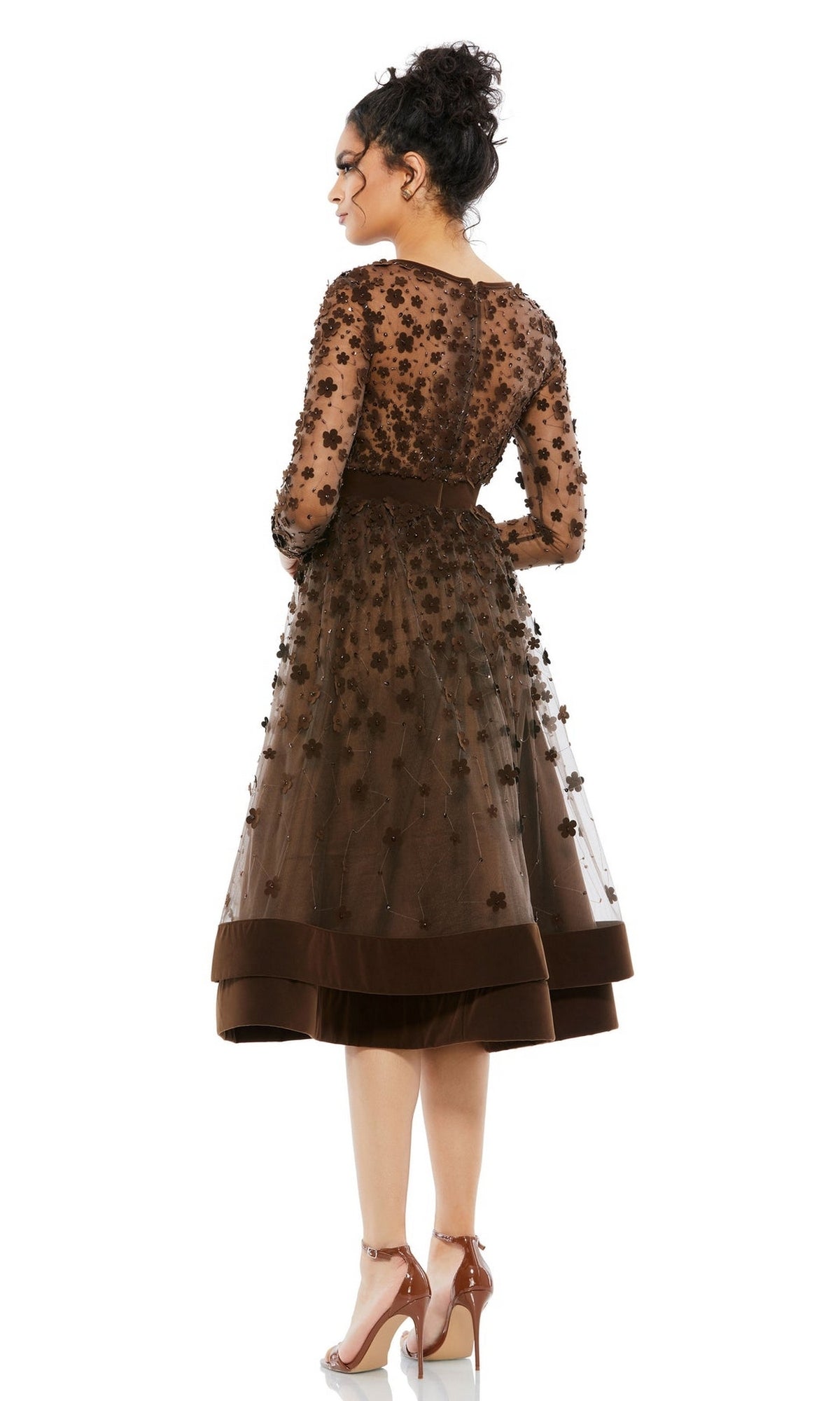 A woman stands with her back to the camera in the Mac Duggal 67007 knee-length wedding-guest dress featuring floral appliqués, sheer sleeves, and high heels.